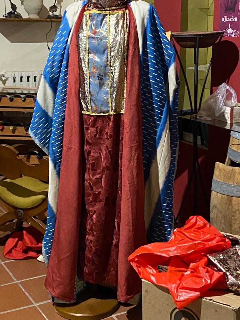 Costume di cortigiana su manichino: mantello a righe blu e bianche sopra un abito rosso con pannello centrale ricamato in oro, ricostruzione della corte di Erode Antipa, 33 d.C.