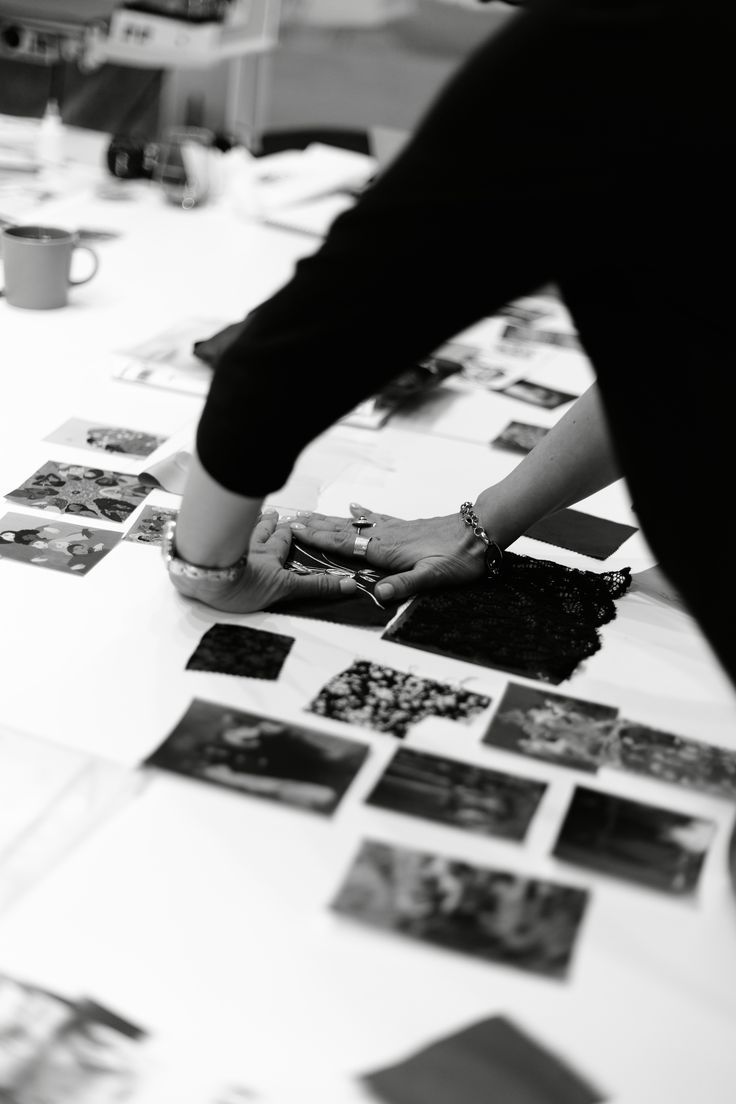 Una docente dispone su un tavolo fotografie di ricerca e campioni di pizzo per comporre la tavola di una collezione.